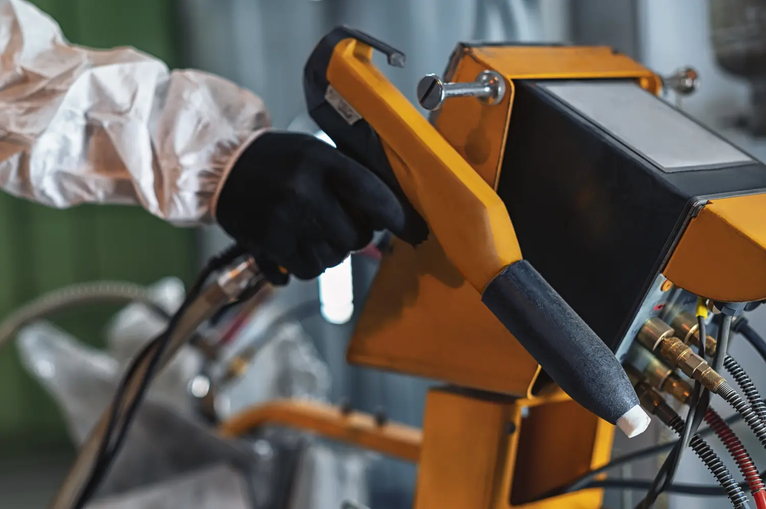Die Hand eines Arbeiters in Schutzkleidung hält ein Pulverbeschichtungssprühgerät