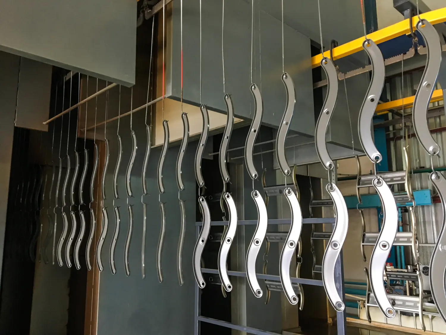 Pulverbeschichtungsanlage. Metallplatten werden an einer Hängeförderstrecke aufgehängt.